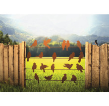 Dekorative Vogel-Silhouetten auf einem Zaun vor einer grünen Landschaft.