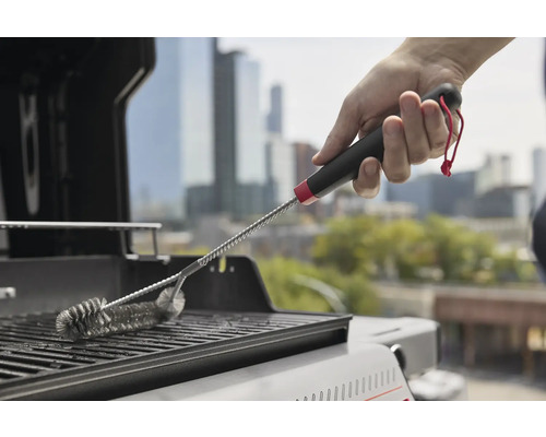 Une main nettoie une grille de barbecue avec une brosse pour barbecue.