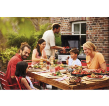 Famille appréciant un repas à table en bois dans le jardin avec barbecue en arrière-plan