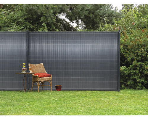 Scène de jardin avec pare-vue, fauteuil en rotin et petite table sur une pelouse