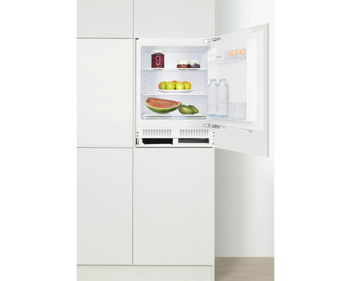 Réfrigérateur intégré avec porte ouverte, rempli de produits alimentaires dans une cuisine blanche