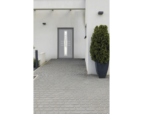 Moderne Haustür mit Glaseinsatz und geraden Edelstahlgriffen in einer hellen Fassade mit Pflastersteinen.