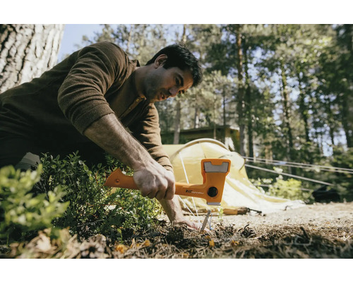 Un homme utilise un marteau pour enfoncer un piquet dans le sol, avec une tente en arrière-plan.