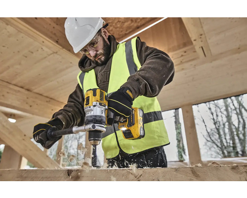 Ein Bauarbeiter bohrt mit einer gelben DeWalt Akku-Bohrmaschine ein Loch in ein Holzbrett.