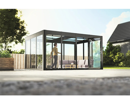 Gewächshaus SunGarden Infinity 4.3 Kunststoff 6 mm 443 x 338 cm anthrazit Freistehender Glasgarten mit Schiebetürsystem und sitzendem Mann auf Terrasse