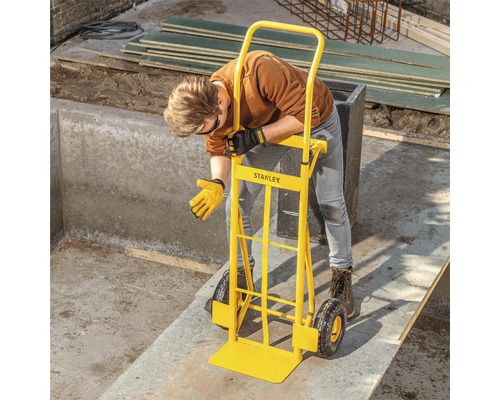 Eine Person benutzt eine gelbe Sackkarre von Stanley, um einen schweren Gegenstand zu bewegen.