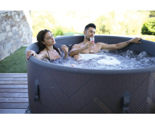 Un couple se détend dans un bain à remous gonflable à l''extérieur avec des boissons.