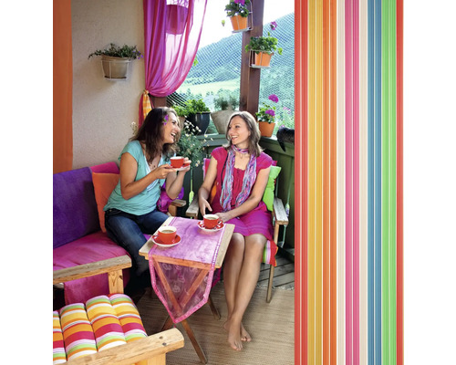Zwei Frauen trinken Kaffee auf einem Balkon mit farbenfroher Dekoration und einem Lamellenvorhang.