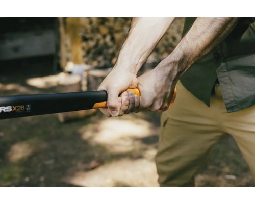 Une personne tient une hache à fendre Fiskars pour fendre du bois.