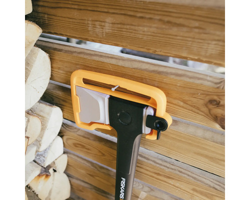 Hache Fiskars avec protège-lame devant une pile de bois