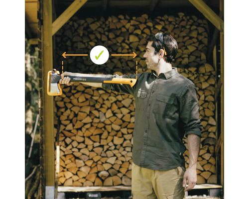 Un homme tient une hache à fendre Fiskars devant une pile de bois pour démontrer la bonne longueur de travail
