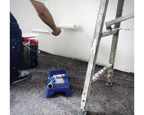 Szene mit Malerarbeiten: Person streicht Wand mit Farbroller, Farbeimer, Farbwanne mit Farbroller und Leiter im Raum.