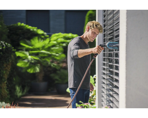 Un homme nettoie des stores avec une brosse et un tuyau d''arrosage dans le jardin.