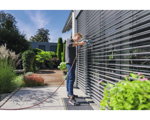 Un homme nettoie des stores extérieurs avec une brosse et un tuyau d''arrosage dans le jardin.
