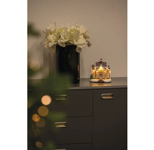 Scène décorative avec vase de fleurs artificielles et maison en pain d''épices illuminée sur une commode.