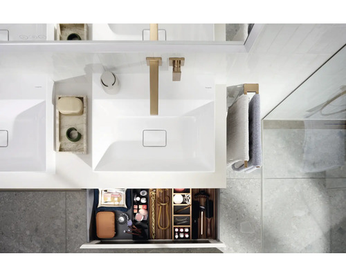 Badezimmeransicht von oben mit Waschbecken, Armaturen und offener Schublade mit Badartikeln.