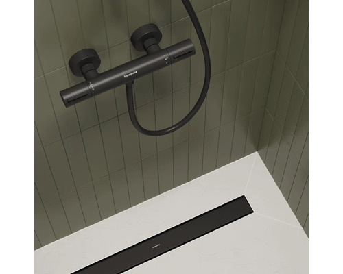 Robinet de douche apparent avec flexible de douche et caniveau de douche dans la zone de douche.