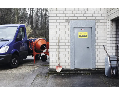 Scène avec bétonnière, camion de chantier, brouette et pelle devant un bâtiment