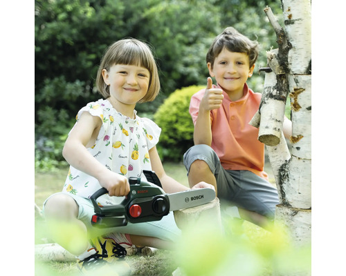 Zwei Kinder spielen mit einer Spielzeugkettensäge der Marke Bosch im Garten.