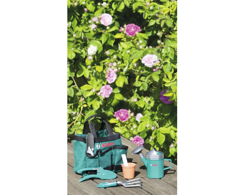 Gartengeräte-Set für Kinder von Bosch mit Tasche, Schaufel, Gartenschere, Harke, Blumentopf und Gießkanne vor blühendem Busch