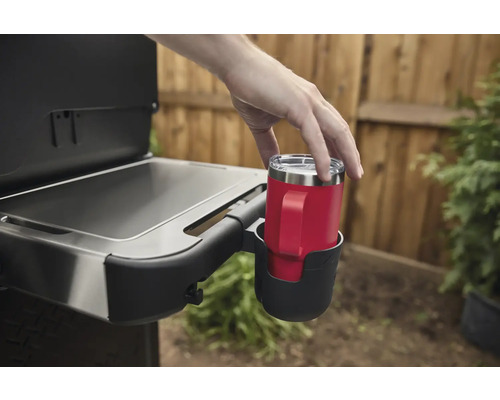 Une personne place une tasse rouge avec une anse dans un porte-gobelet sur un gril.