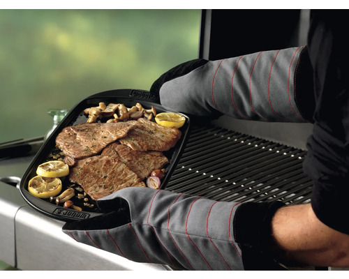 Un homme portant des gants de barbecue tient un plat de grillade avec de la viande, du citron et des champignons au-dessus d''un barbecue.