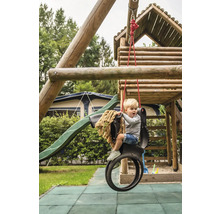 Garçon sur une balançoire à pneus devant une tour de jeux avec toboggan dans le jardin