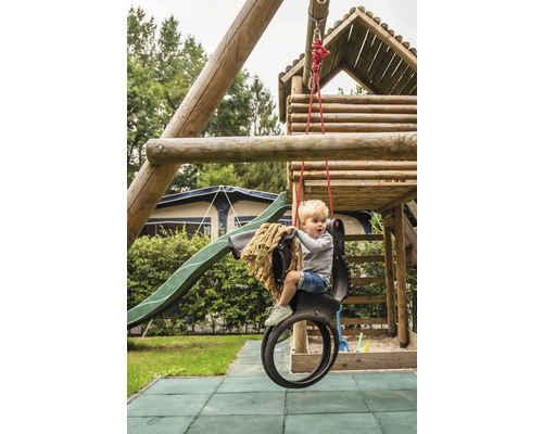 Garçon sur une balançoire à pneus devant une tour de jeux avec toboggan dans le jardin