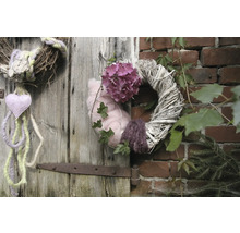 Des couronnes décoratives sont suspendues à une porte en bois et à un mur de briques, ornées de fleurs, de cœurs et de plantes.