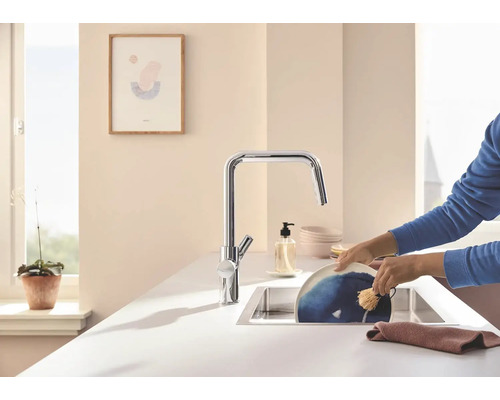 Küchenspüle mit Einhebelmischer und Person beim Abwaschen eines Tellers