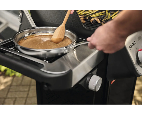 Sur un gril, une sauce est préparée dans une poêle en acier inoxydable avec une cuillère en bois.