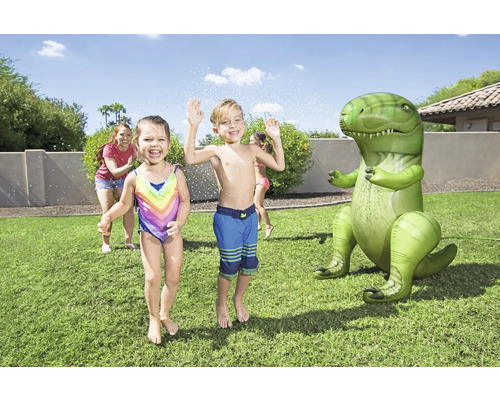Des enfants jouent avec un arroseur de jardin dinosaure gonflable sur une pelouse.