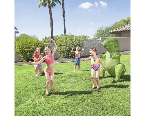 Des enfants jouent avec un arroseur d''eau dinosaure gonflable dans le jardin.