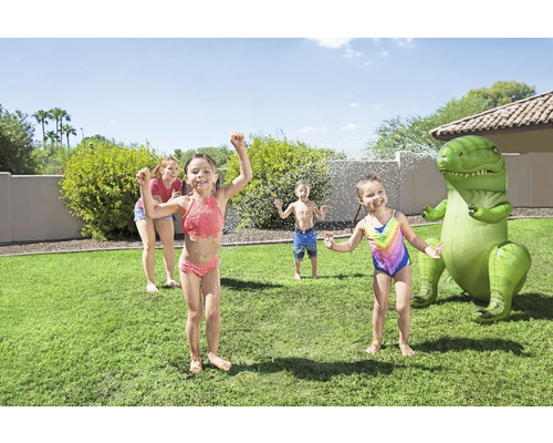 Des enfants jouent avec un arroseur dinosaure gonflable dans le jardin.