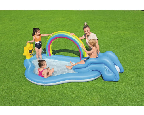 Aufblasbares Planschbecken mit Regenbogen, Rutsche und spielenden Kindern auf einer Rasenfläche