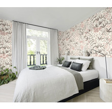 Chambre à coucher avec lit devant un papier peint à motifs floraux et une fenêtre avec des rideaux.