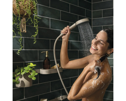 Frau benutzt Handbrause in der Dusche mit Aufbewahrungsregal und Pflanzen