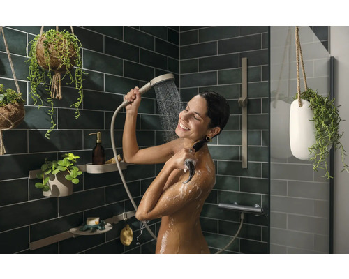 Frau unter der Dusche mit Handbrause, umgeben von Pflanzen
