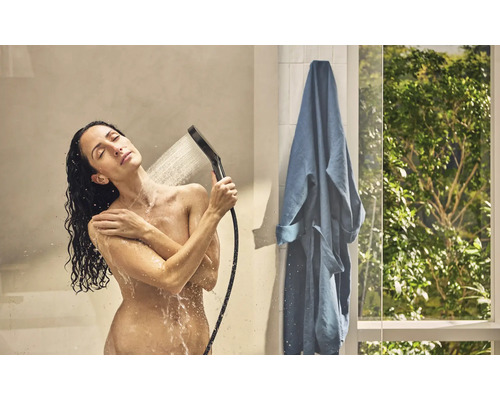 Frau unter der Dusche mit Handbrause und Bademantel im Badezimmer.