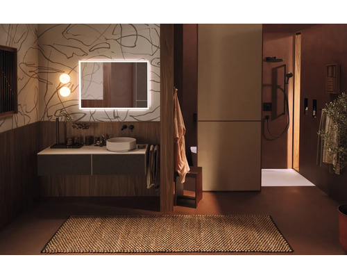 Helles Badezimmer mit Waschtisch, beleuchtetem Spiegel und begehbarer Dusche.