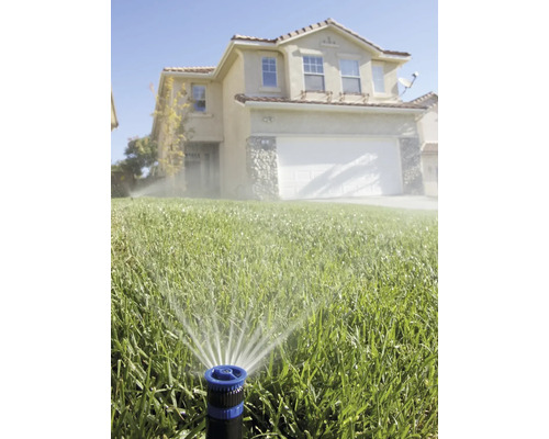 Rasensprenger bewässert Rasenfläche vor Wohnhaus