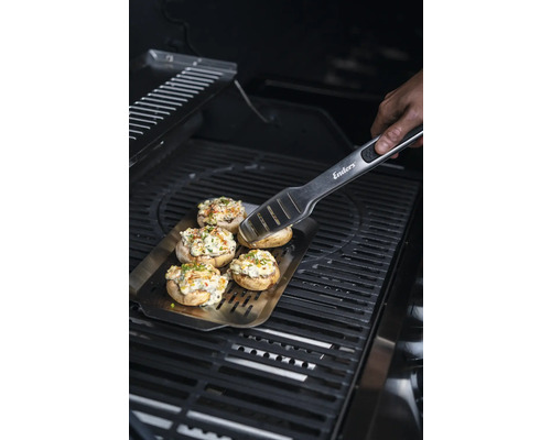 Gefüllte Champignons auf einer Grillplatte mit Grillzange auf einem Grill