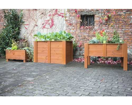 Trois bacs à fleurs en bois plantés devant un mur en briques