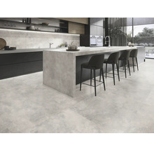 Cuisine moderne avec carrelage au sol aspect béton, îlot de cuisine et tabourets de bar.