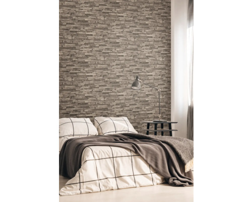 Chambre à coucher avec papier peint aspect pierre, lit, table de chevet et lampe.