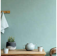 Scène avec table, théière, tasses, plante et serviette devant un mur structuré