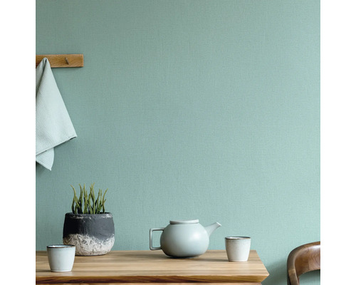 Szene mit Tisch, Teekanne, Tassen, Pflanze und Handtuch vor einer strukturierten Wand