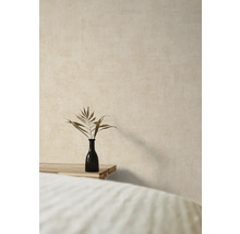 Vase décorative avec branche de plante sur une table en bois devant un mur texturé.