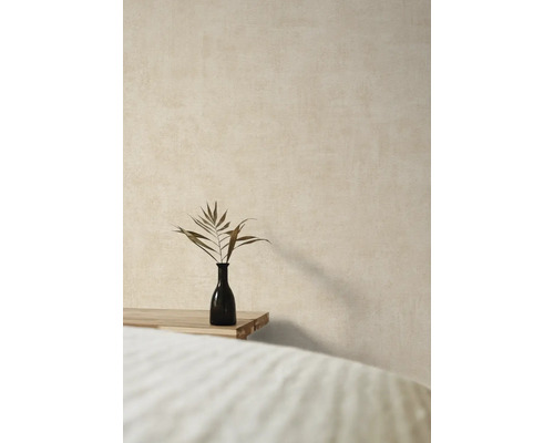 Vase décorative avec branche de plante sur une table en bois devant un mur texturé.