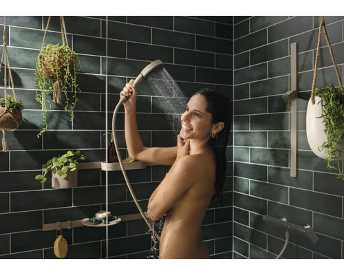 Frau unter der Dusche mit Handbrause in einem Badezimmer mit grünen Fliesen und Pflanzen